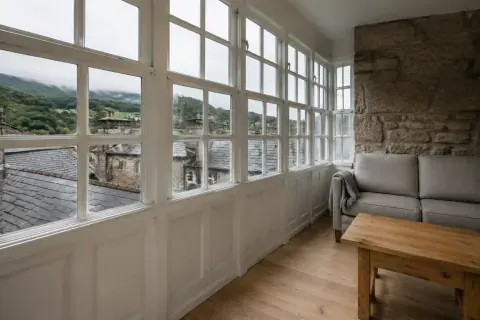 Salón de un apartamento con galería acristalada de madera y vistas a los tejados de pizarra