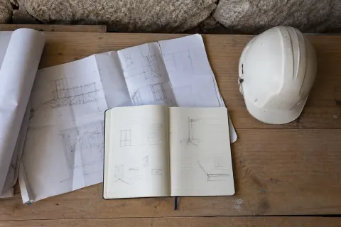 Cuaderno técnico abierto junto a planos de ejecución y un casco de obra
